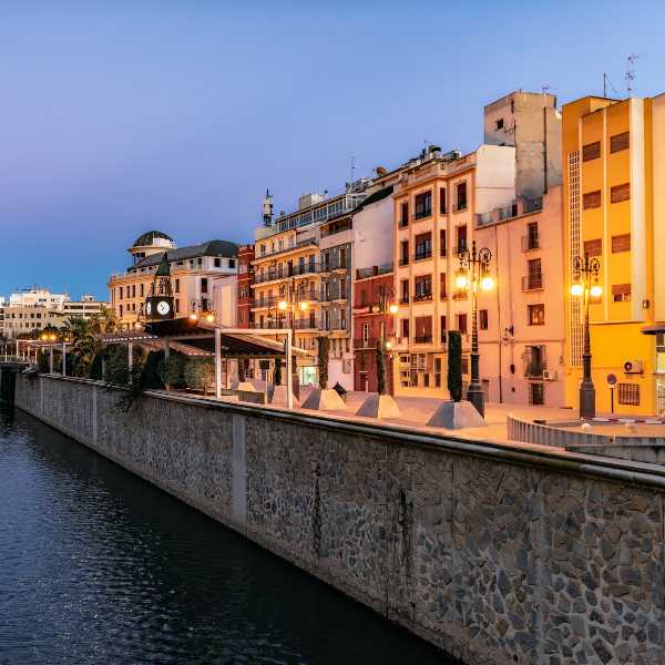 Vista del río y edificios iluminados en Orihuela al atardecer.